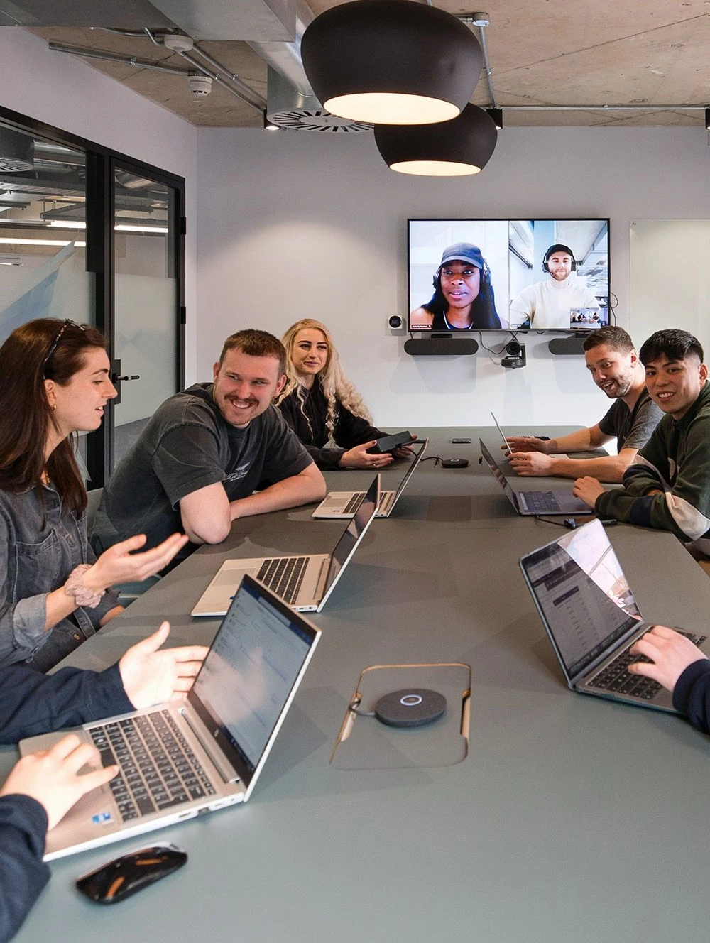 The Grabll team around a meeting table with laptops, two teammates joining on a video call.